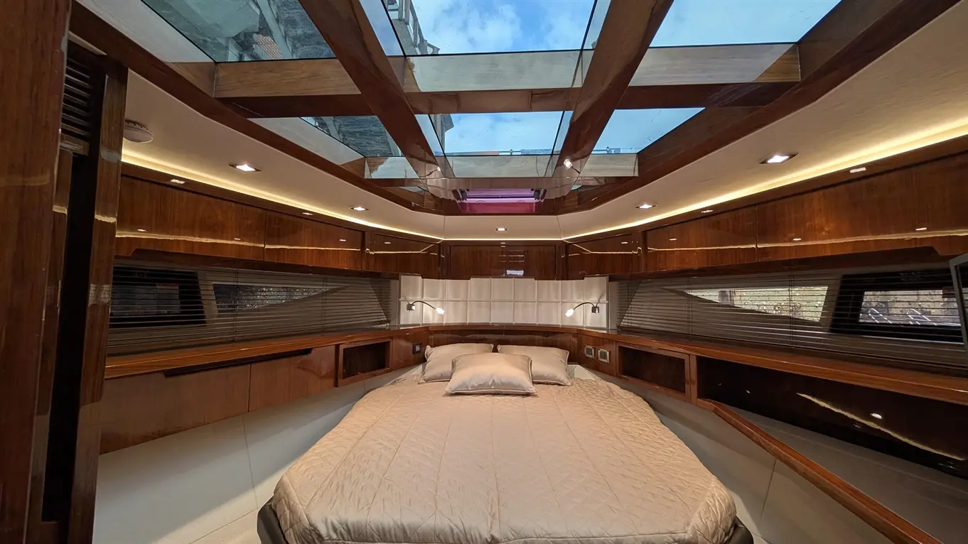 Luxurious yacht bedroom featuring a king-size bed, wooden cabinetry, and a glass ceiling, illuminated by soft lighting.